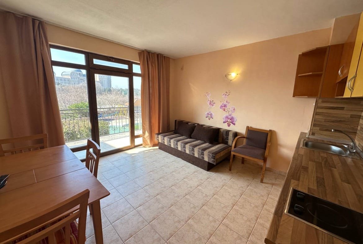 Современный двухкомнатный апартамент: кухня, зона отдыха с диваном, стол для обедов и выход на балкон с видом на природу.