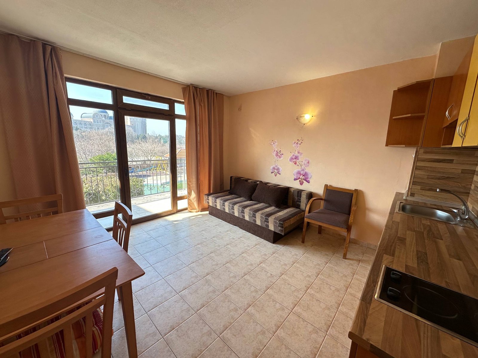 Современный двухкомнатный апартамент: кухня, зона отдыха с диваном, стол для обедов и выход на балкон с видом на природу.