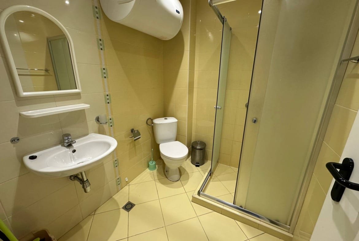 Современная ванная комната в студии с душевой кабиной, унитазом и раковиной на желтых плитках.