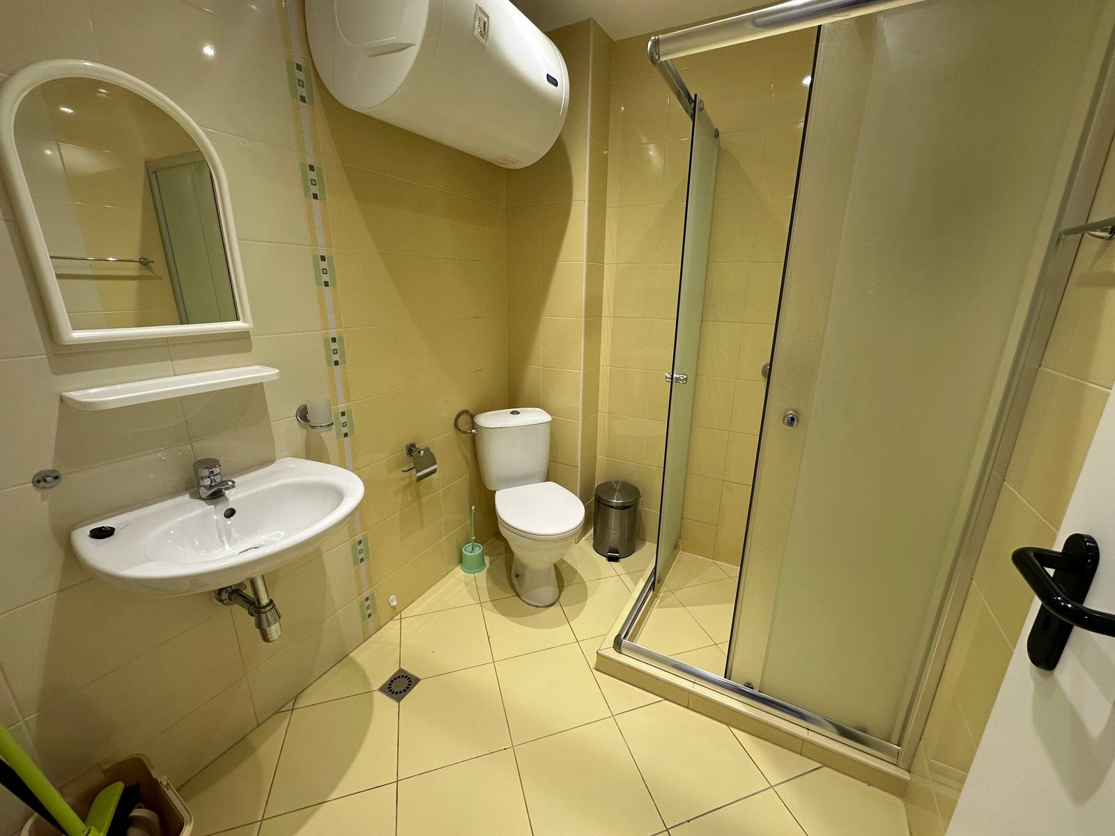 Современная ванная комната в студии с душевой кабиной, унитазом и раковиной на желтых плитках.