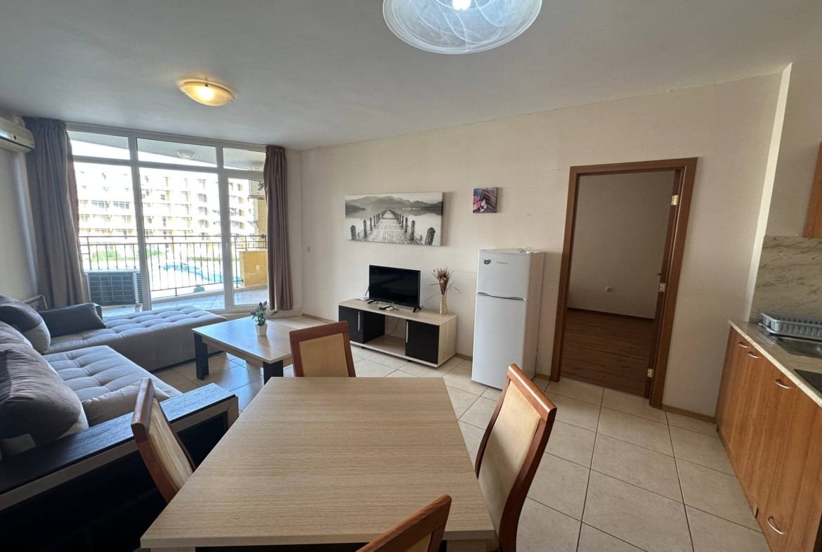 Современная гостиная с кухней, диваном, телевизором и обеденным столом, выход на балкон с видом на улицу.