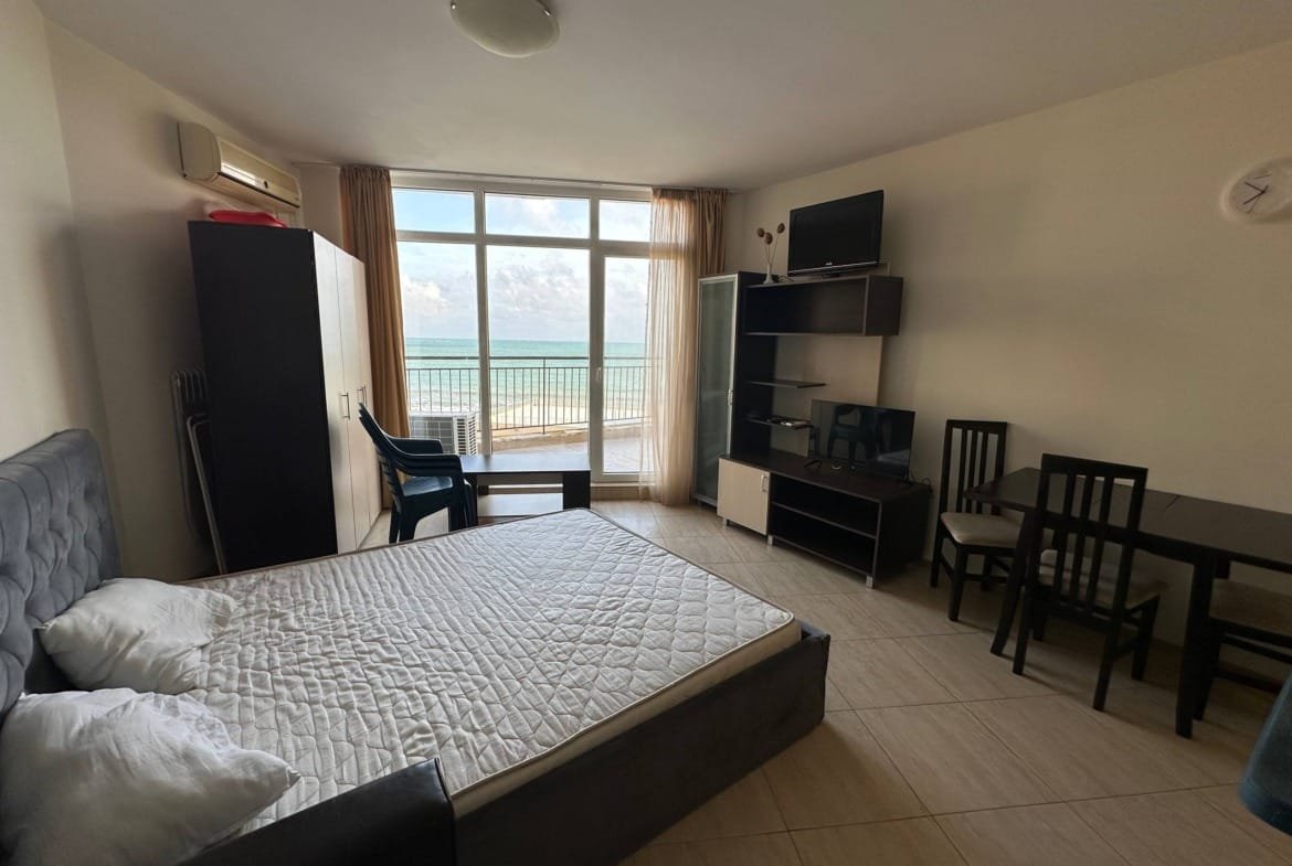 Современная студия с панорамным окном, кроватью, столом, стульями и телевизором, выходящая на море в комплексе “Midia Family Resort”.