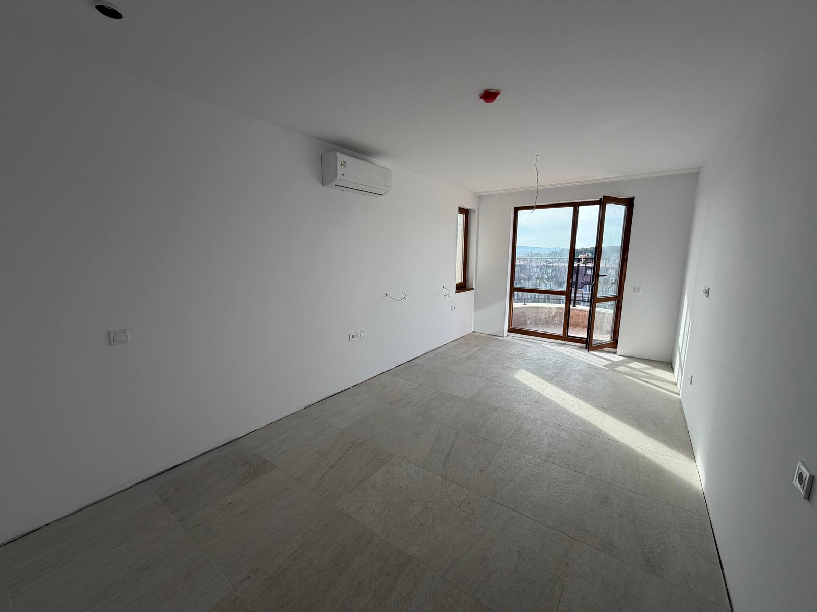 Просторная студия с большими окнами и видом, свежий ремонт, плиточный пол, кондиционер на стене.