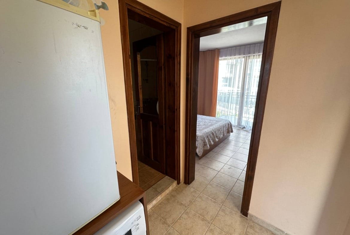 Вход в двухкомнатный апартамент с кухней, ванной и спальней, светлые тона, плиточный пол и большие окна.