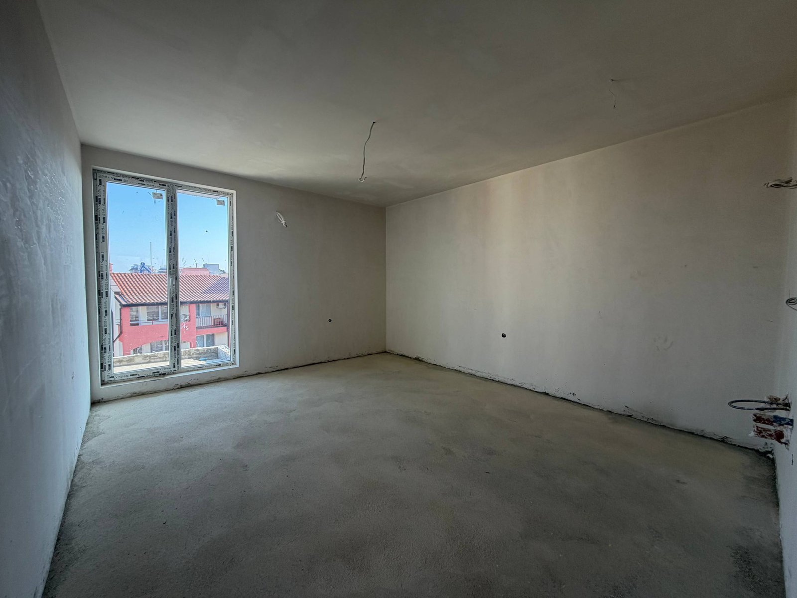 Пустая студия с окнами на улицу, белые стенами и светлым полом, готовая для отделки в комплексе La Mer Gold.