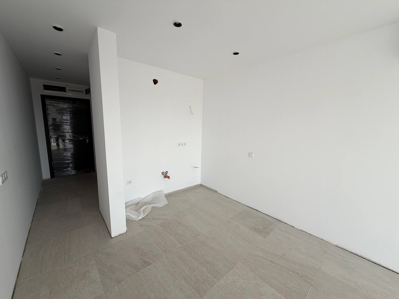 Современно оформленная комната с белыми стенами, плиточным полом, без мебели и декора, готовая для дальнейших работ.