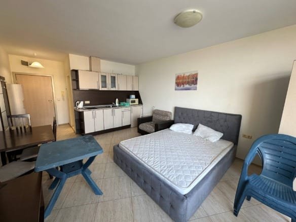 Комната студии с кухонным уголком, диваном и обеденной зоной, светлые тона отделки, современная мебель.