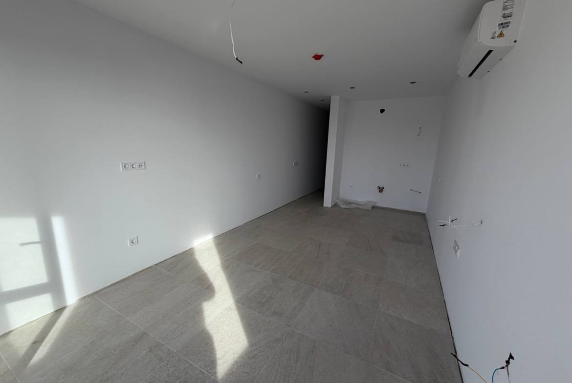 Современная студия с ровными стенами, светлыми плиточными полами и большими окнами, готовая к отделке.