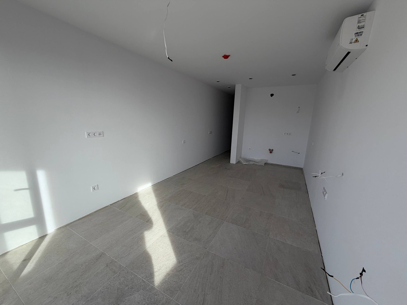 Современная студия с ровными стенами, светлыми плиточными полами и большими окнами, готовая к отделке.