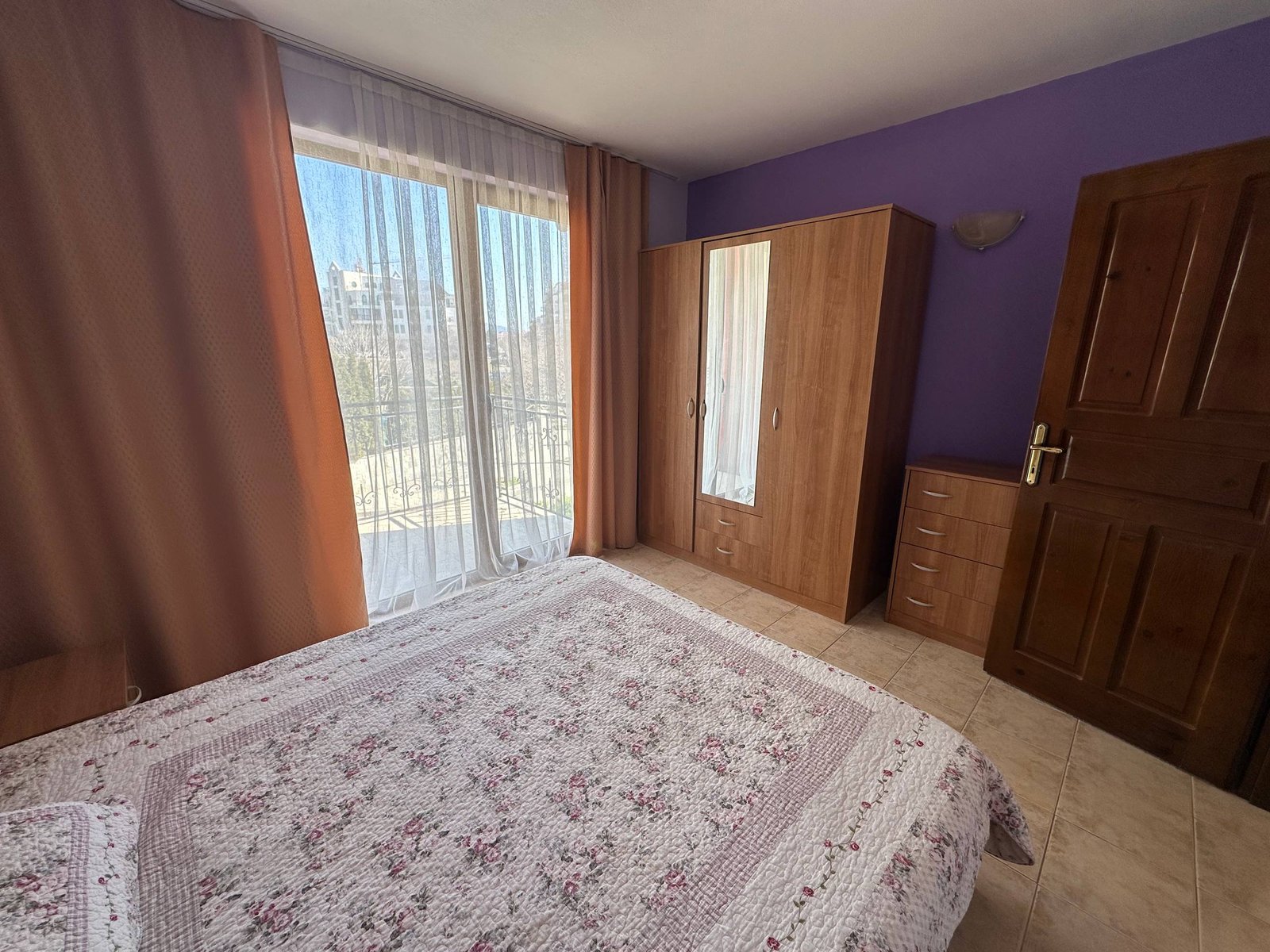 Двухкомнатный апартамент с балконом, светлыми шторами и деревянной мебелью, оформленный в теплых нюансах.