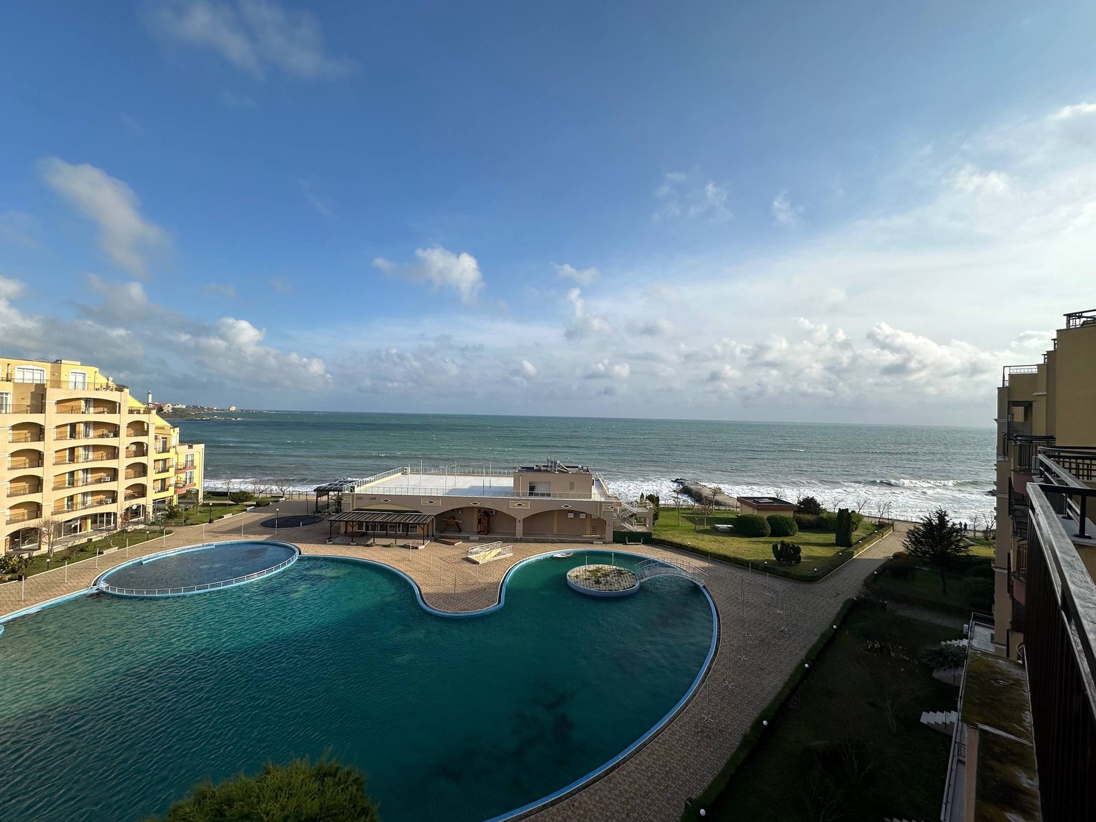 Вид на море и бассейн комплекса Midia Family Resort, окруженный зелеными насаждениями и зданиями на побережье.