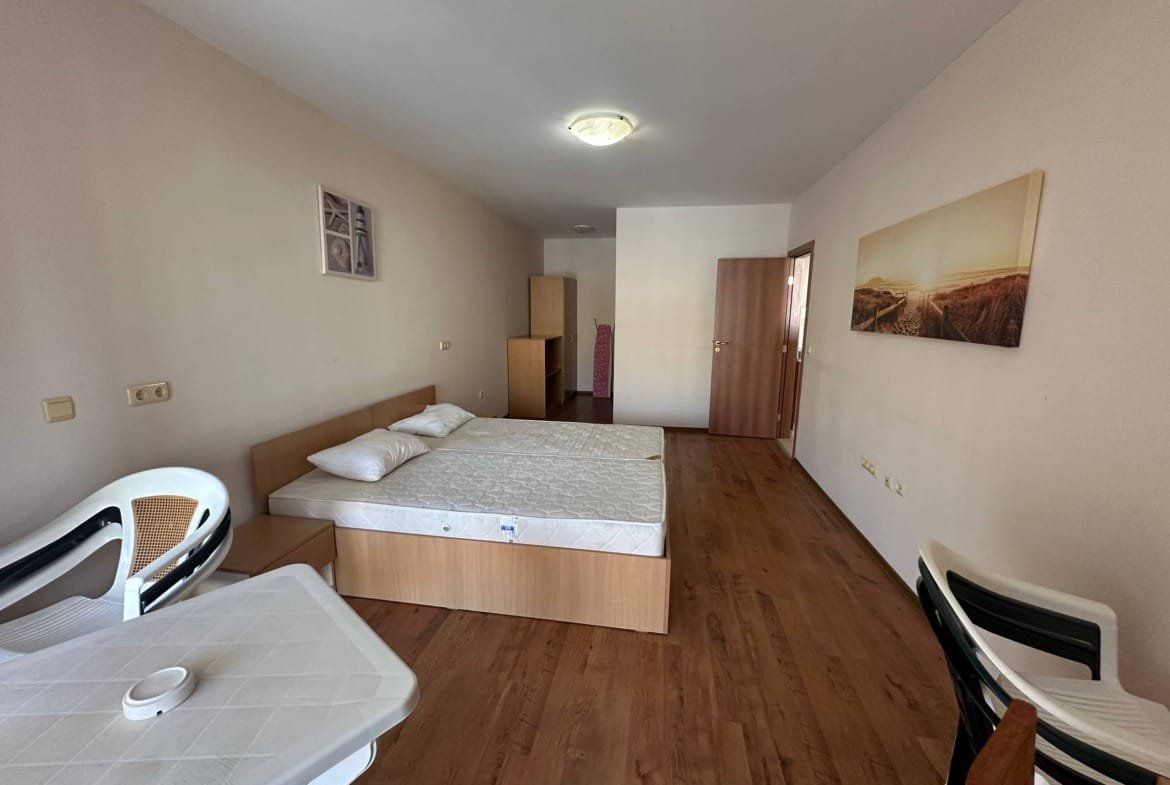 Однокомнатный номер с деревянным полом, кроватью без постельного белья, столом и стульями, украшен картинами.