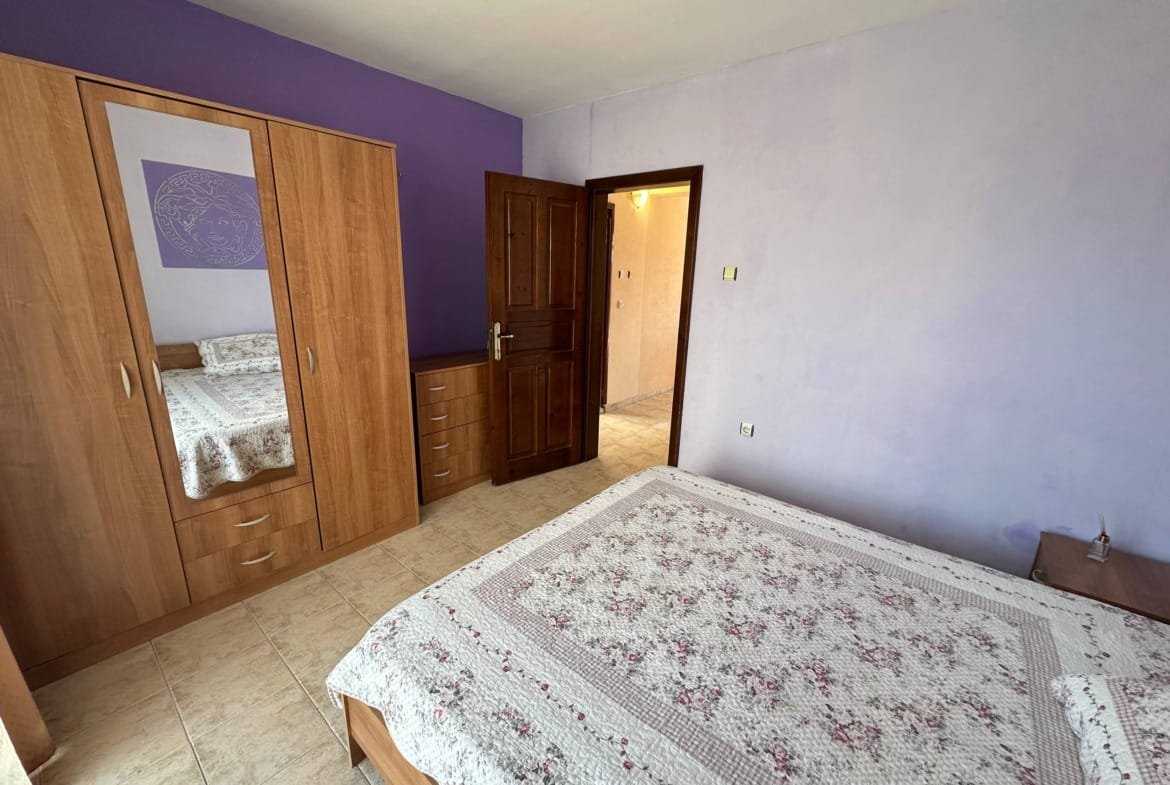 Комната с двуспальной кроватью, комодом и зеркальным шкафом, стены окрашены в светло-фиолетовый цвет.