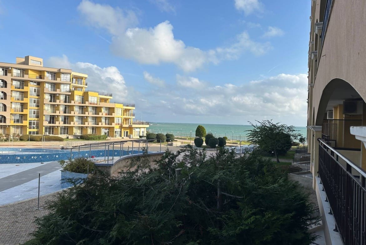 Вид на жилой комплекс у моря с бассейном и зелеными насаждениями на фоне голубого неба и облаков.