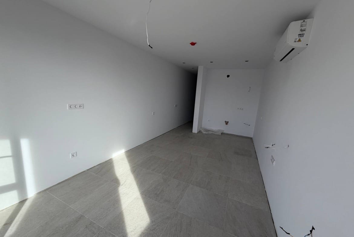 Современная студия в комплексе с белыми стенами, светлым плиточным полом и большими окнами, готовая к отделке.