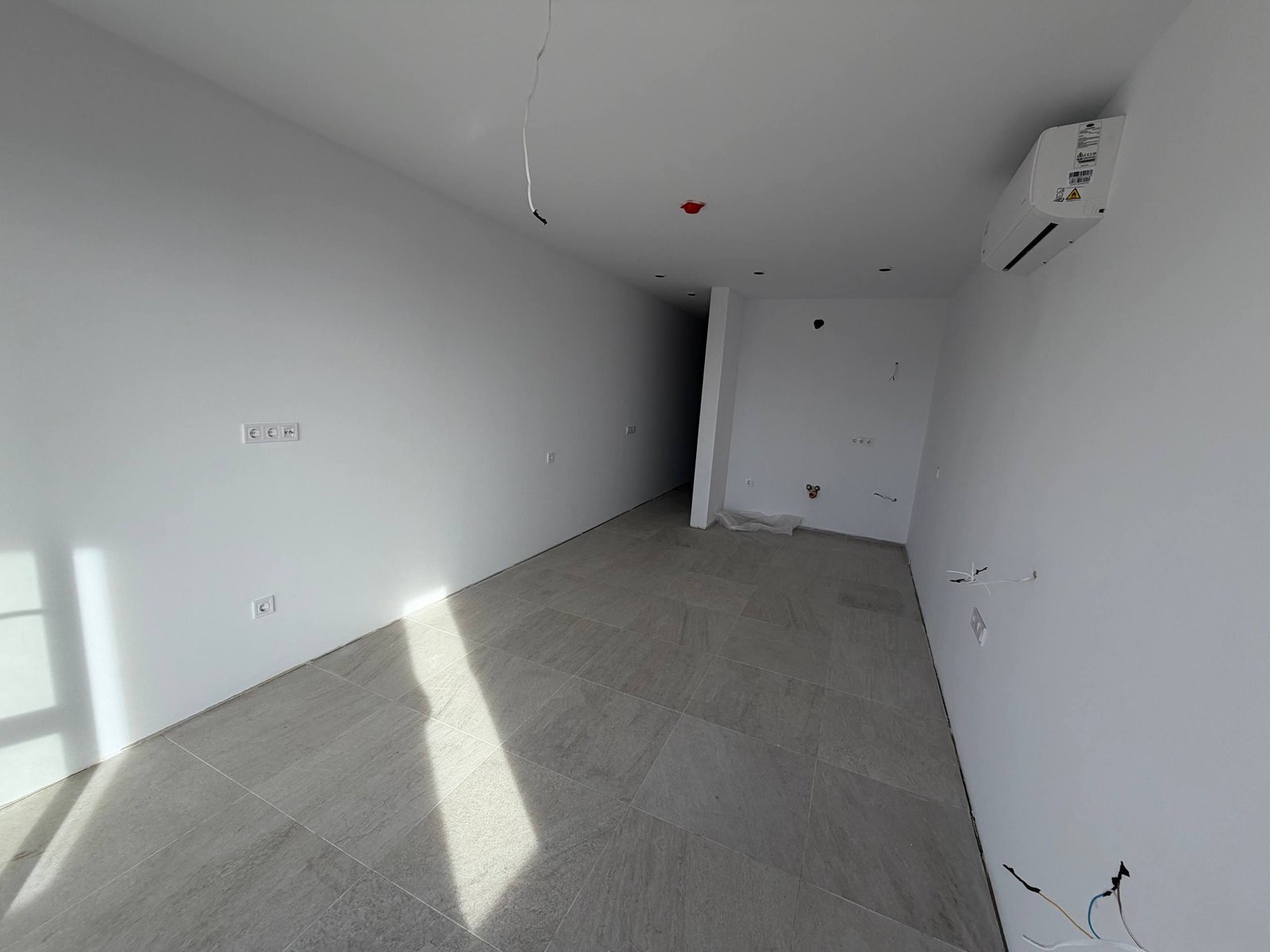 Современная студия в комплексе с белыми стенами, светлым плиточным полом и большими окнами, готовая к отделке.