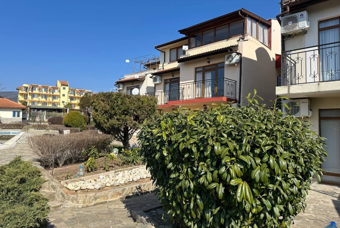 Двухкомнатный апартамент в комплексе Yalta, яркое небо, зелёные насаждения и ухоженный ландшафт вокруг здания.