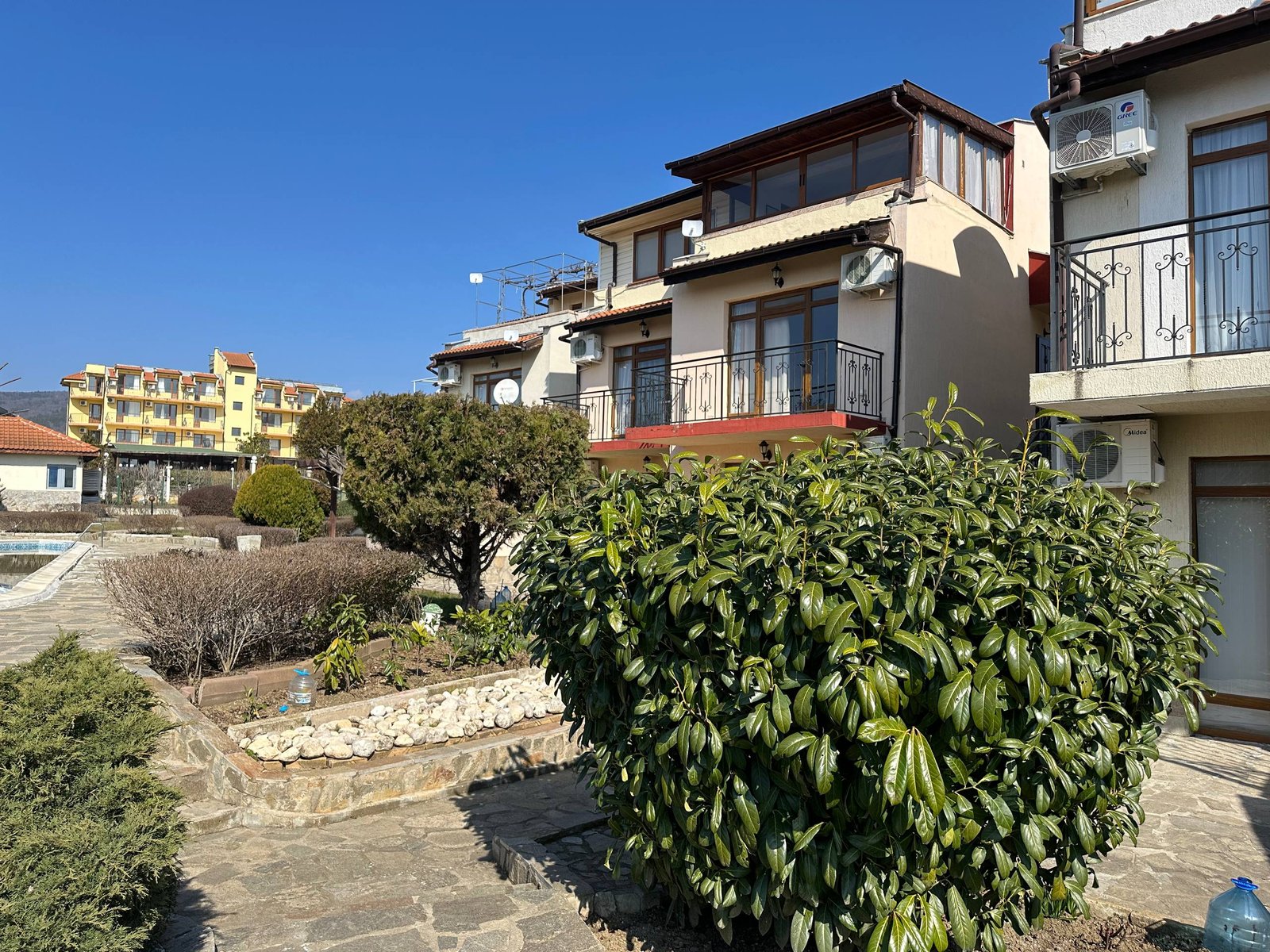 Двухкомнатный апартамент в комплексе Yalta, яркое небо, зелёные насаждения и ухоженный ландшафт вокруг здания.