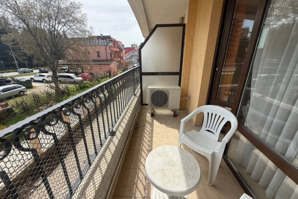 Уютный балкон с белыми пластиковыми стульями и столом, вид на улицу и окружающие дома в Болгарии, пригодный для отдыха.