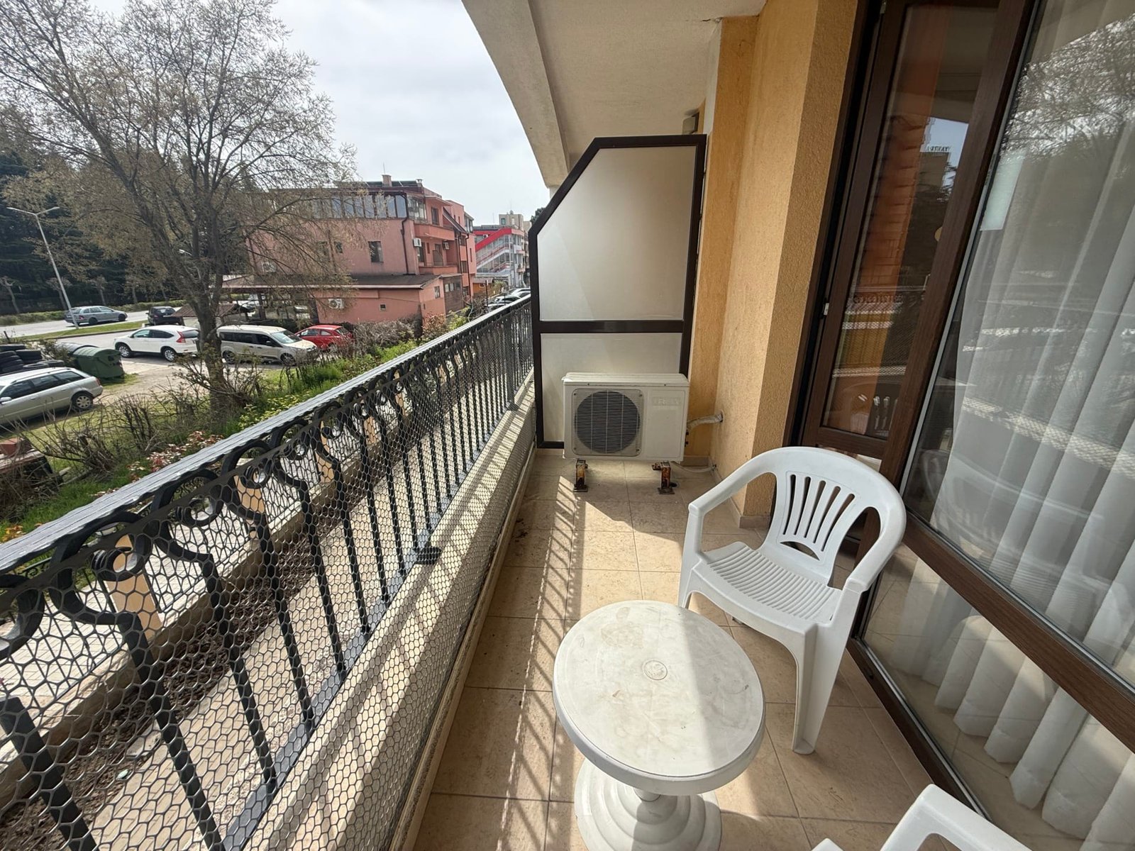 Уютный балкон с белыми пластиковыми стульями и столом, вид на улицу и окружающие дома в Болгарии, пригодный для отдыха.