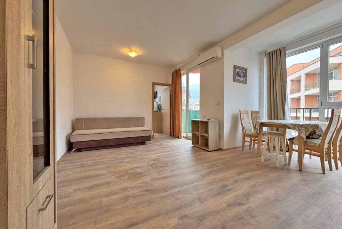 Современная квартира в Святом Власе, светлая гостиная с диваном и обеденным столом, большие окна с видом на улицу.