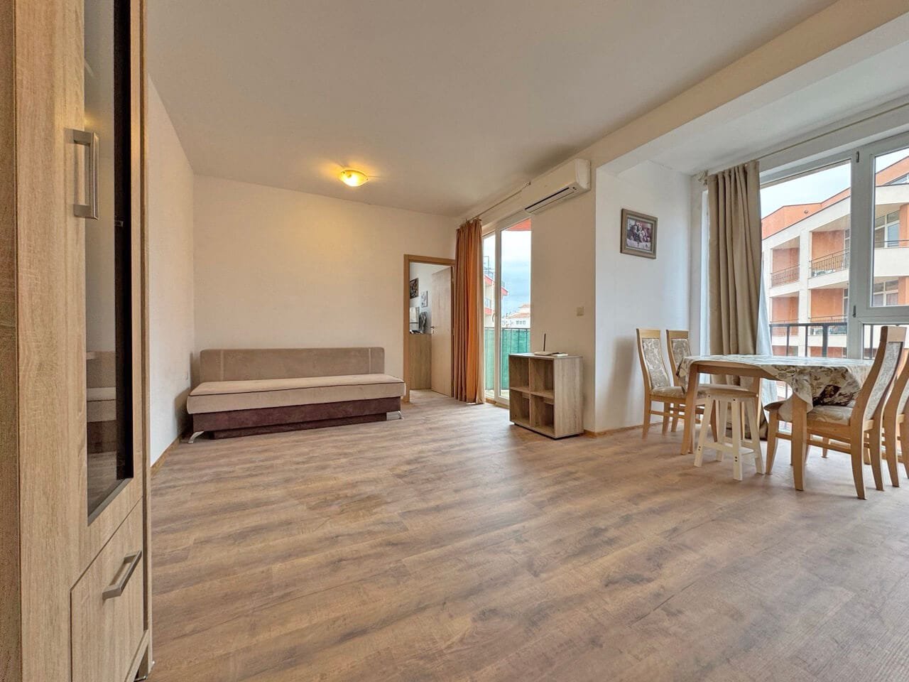 Современная квартира в Святом Власе, светлая гостиная с диваном и обеденным столом, большие окна с видом на улицу.