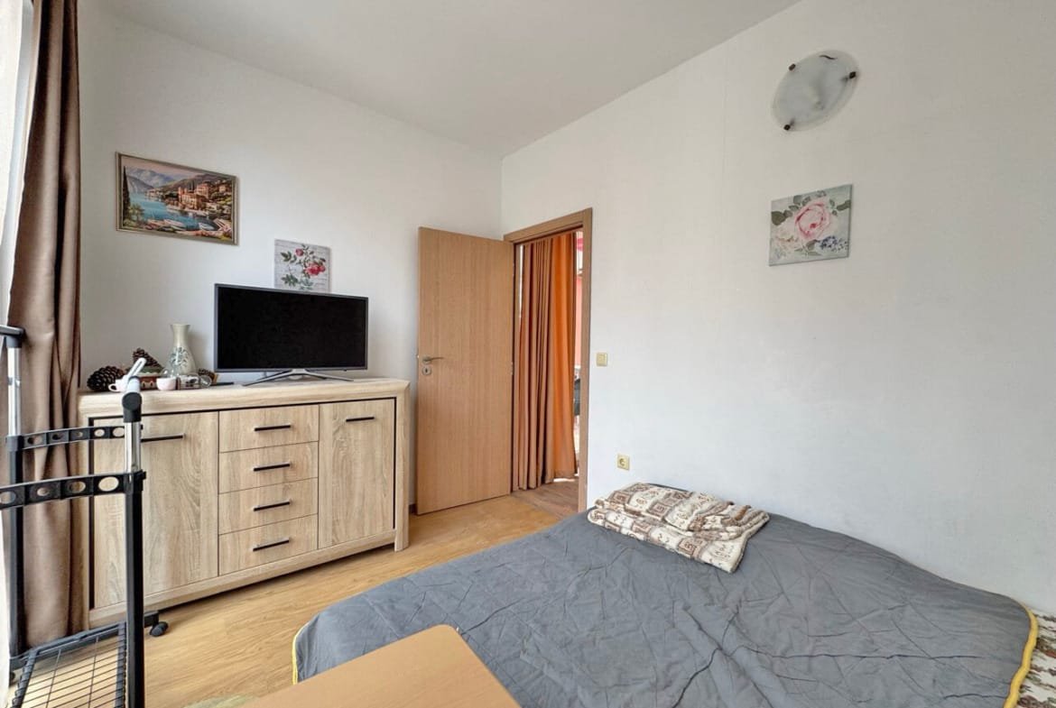 Уютная спальня с комодом, телевизором и выходом на террасу в квартире на Солнечном берегу. Идеально для отдыха у моря.