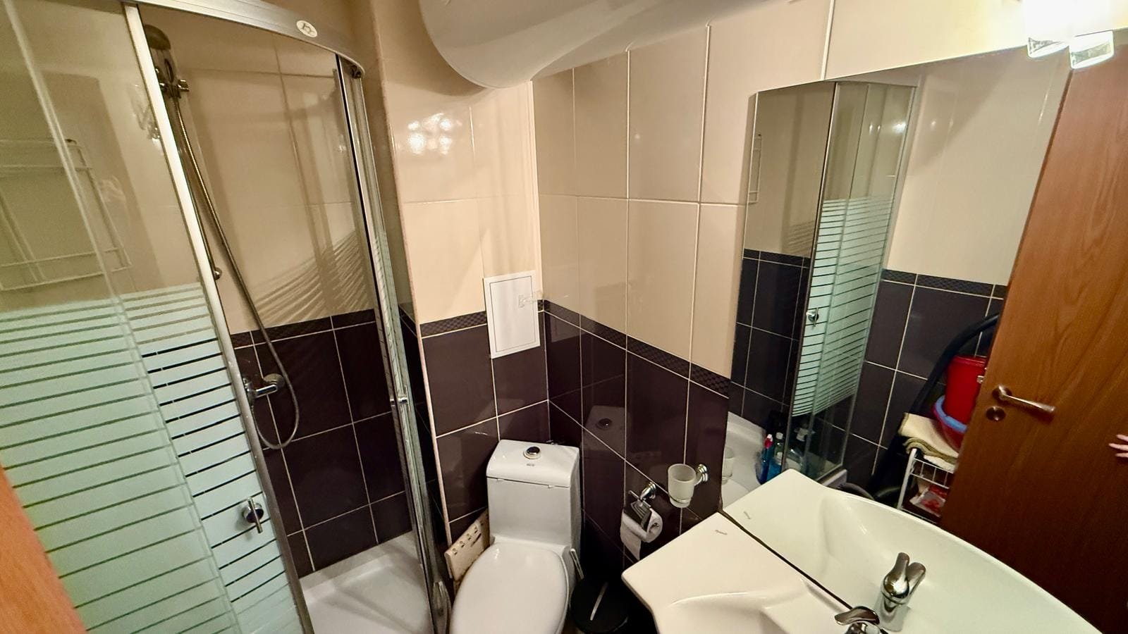 Современная ванная комната с душевой кабиной, унитазом и раковиной, оформленная в светлых и темных тонах для удобства.