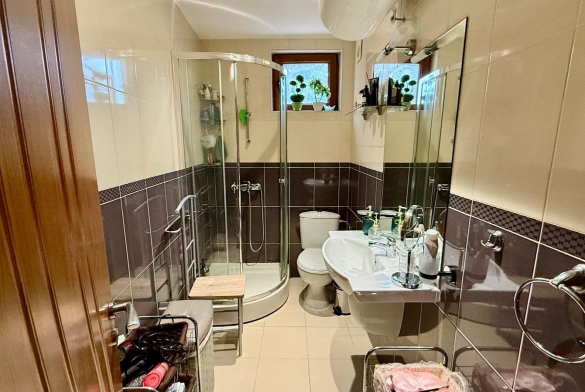 Светлая ванная комната с душевой кабиной, унитазом и раковиной, оформленная в современных тонах, подходит для жилья в Болгарии.