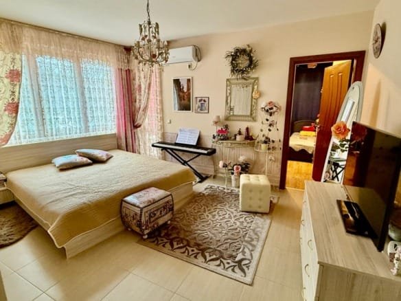 Современная спальня с двуспальной кроватью, красивыми шторами и телевизором, стильный интерьер для комфортной жизни в Болгарии.