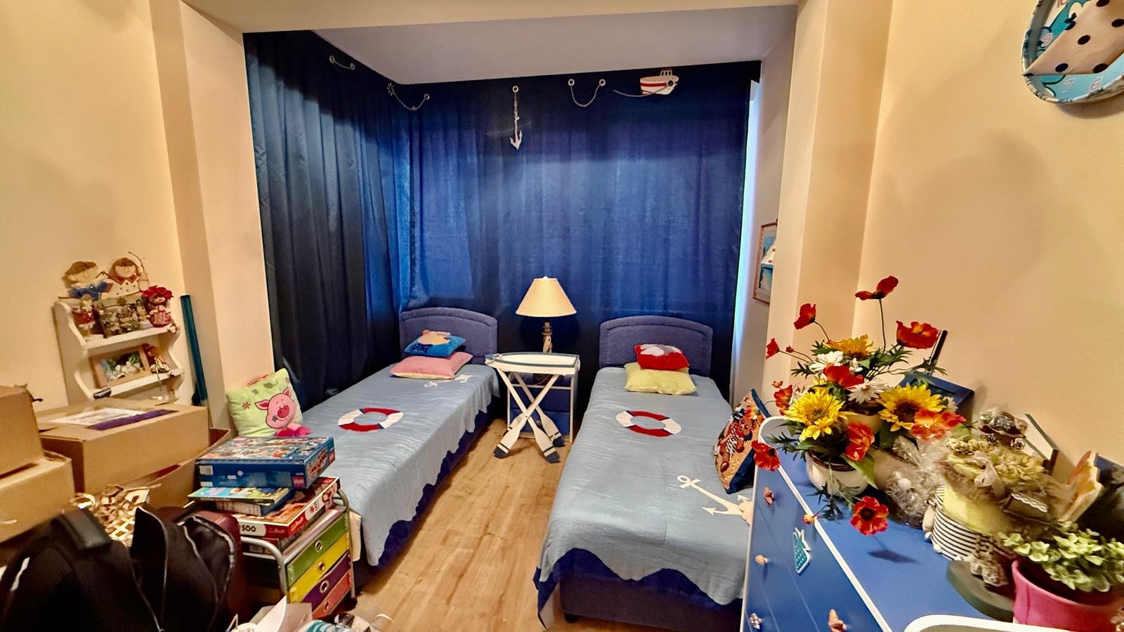 Комната с двумя одиночными кроватями, синими шторами и яркими декорациями, идеально подходит для аренды недвижимости в Болгарии.