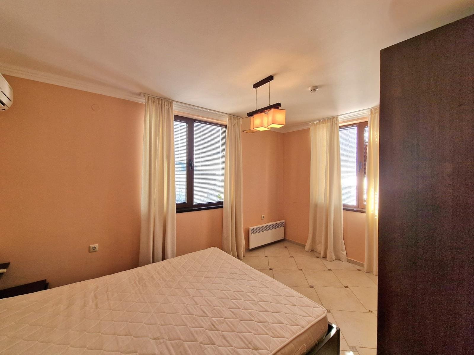 Светлая спальная комната с окнами, пастельные тона, пустая кровать и мягкие curtains, идеальна для покупки недвижимости в Болгарии.