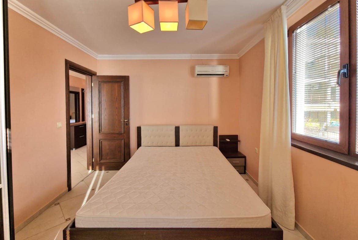 Современная спальня с кроватью, светлыми стенами и кондиционером, подходящая для покупки недвижимости в Болгарии.