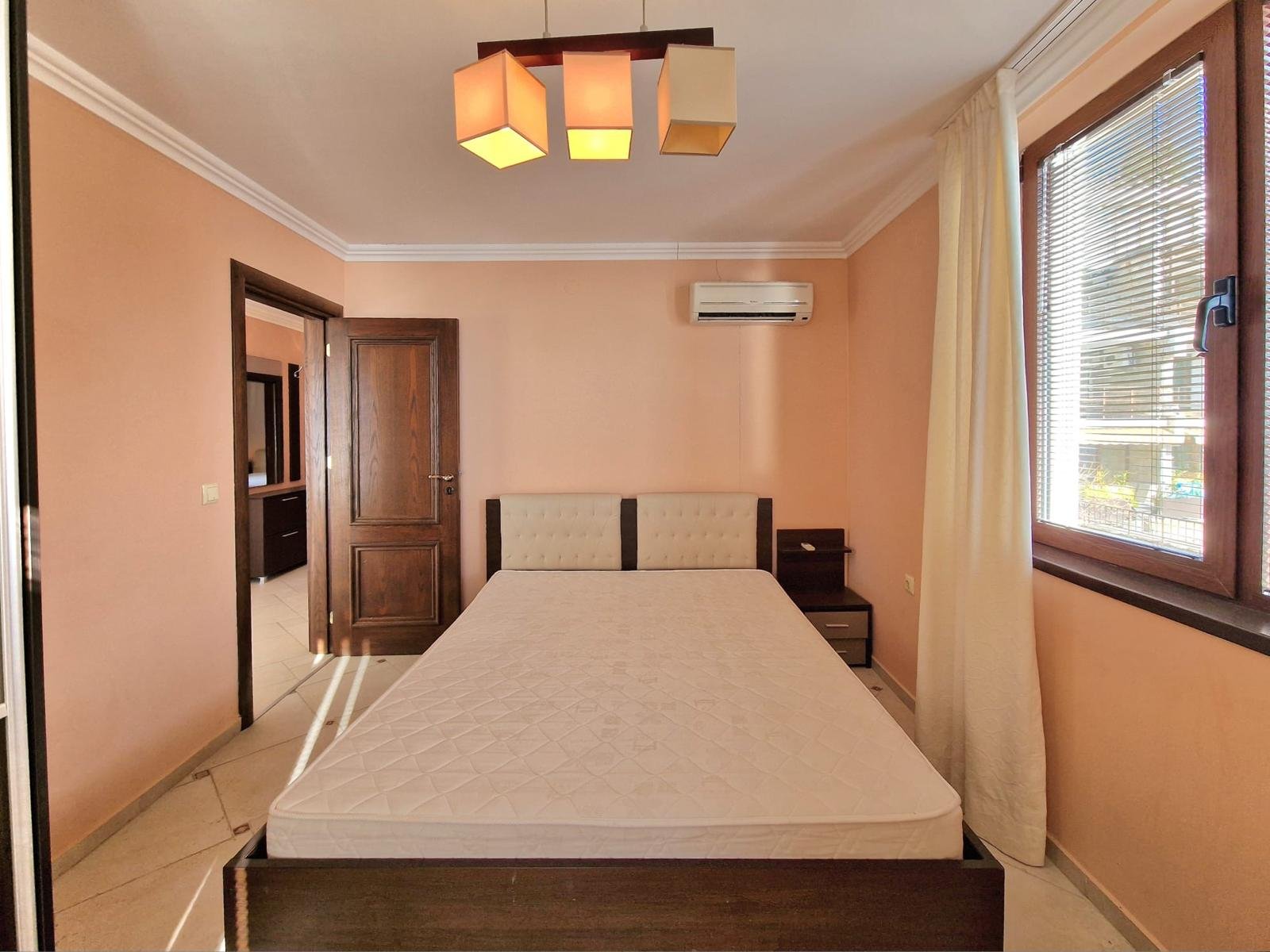 Современная спальня с кроватью, светлыми стенами и кондиционером, подходящая для покупки недвижимости в Болгарии.