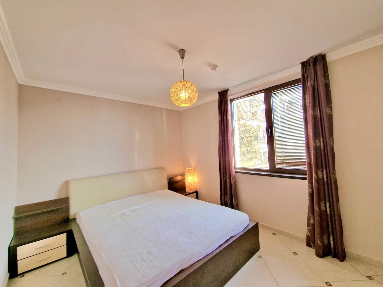 Светлая спальня с двойной кроватью, прикроватными тумбочками и большим окном, предлагающая уютную атмосферу для отдыха.