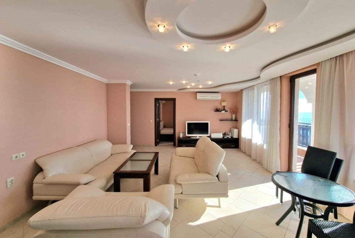 Современная гостиная с мягкой мебелью, телевизором и балконом, идеальная для комфортной жизни в Болгарии.