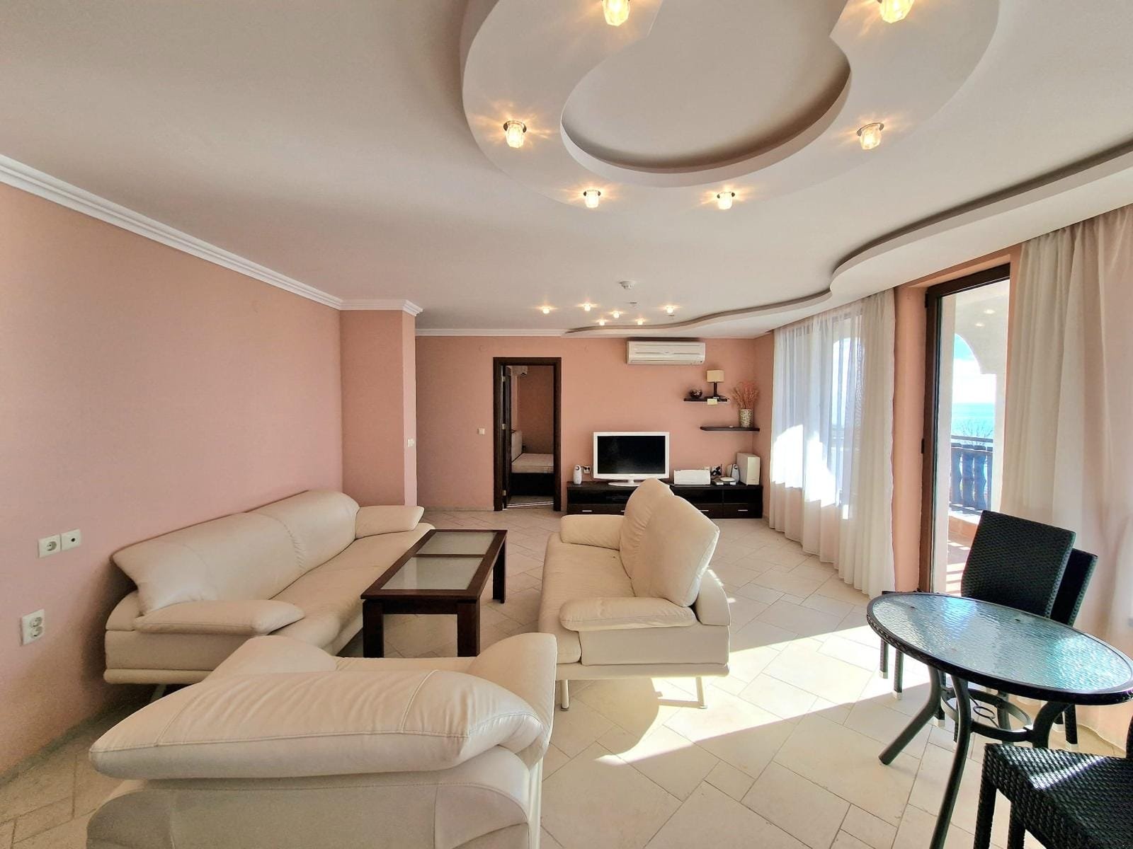 Современная гостиная с мягкой мебелью, телевизором и балконом, идеальная для комфортной жизни в Болгарии.