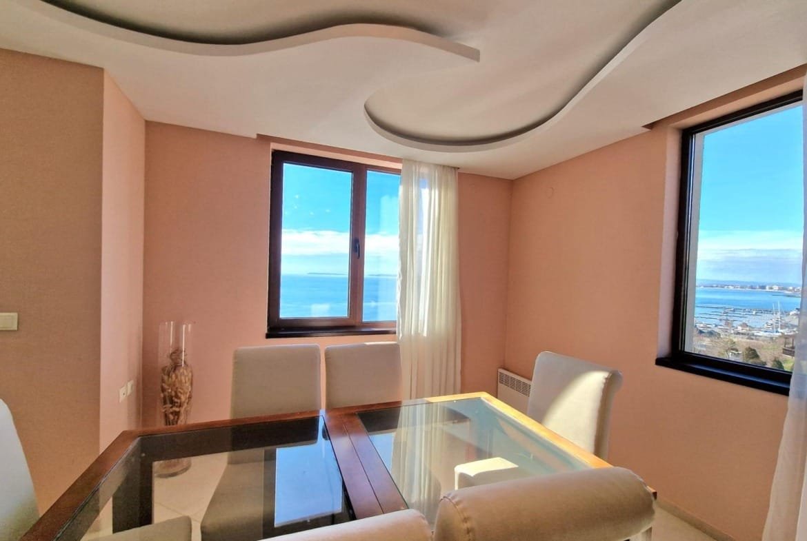 Светлая гостиная с панорамным окном, столом и стульями, предлагающая вид на море в Болгарии. Идеальное место для отдыха.