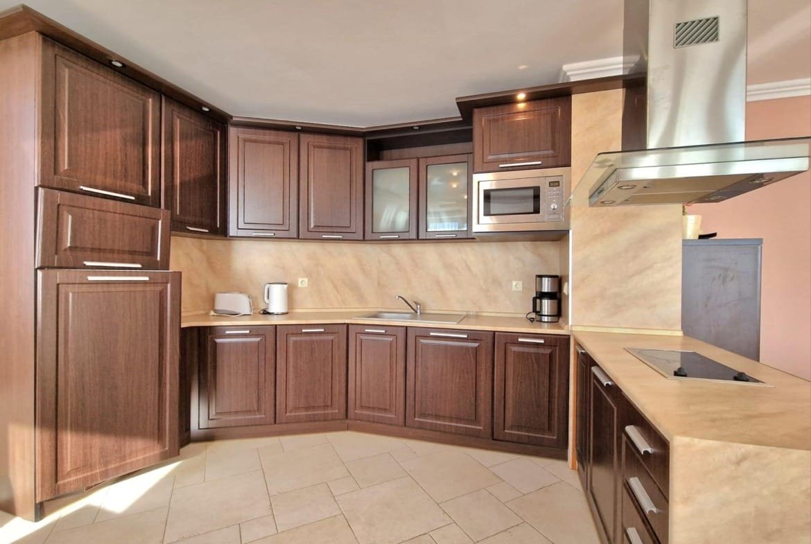 Современная кухня с деревянными шкафами и встроенной техникой, идеальна для продажи недвижимости в Болгарии.