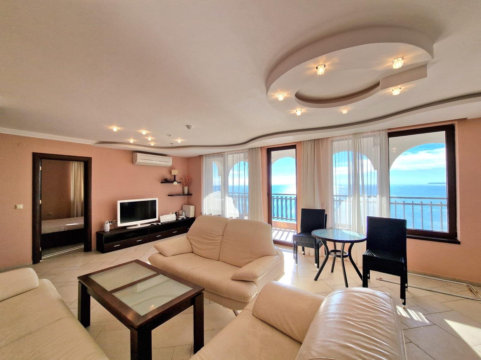 Современная гостиная с панорамными окнами, мебелью и видом на море, идеальное пространство для отдыха в Болгарии.