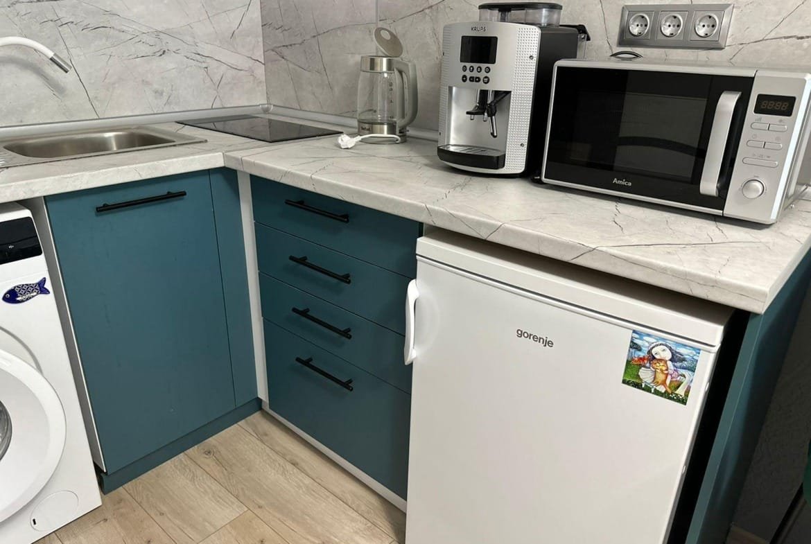 Кухня с белым холодильником, кофемашиной и микроволновкой на мраморной столешнице, выполненной в голубых тонах.