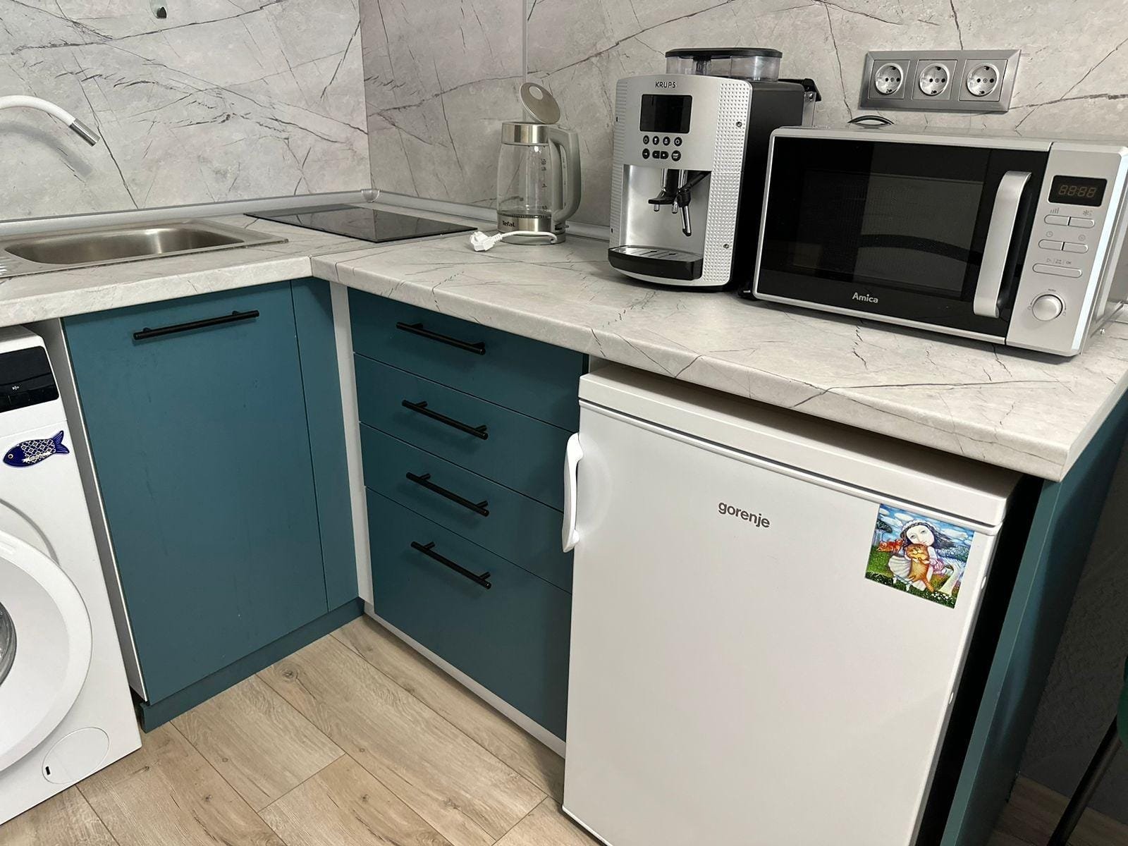 Кухня с белым холодильником, кофемашиной и микроволновкой на мраморной столешнице, выполненной в голубых тонах.