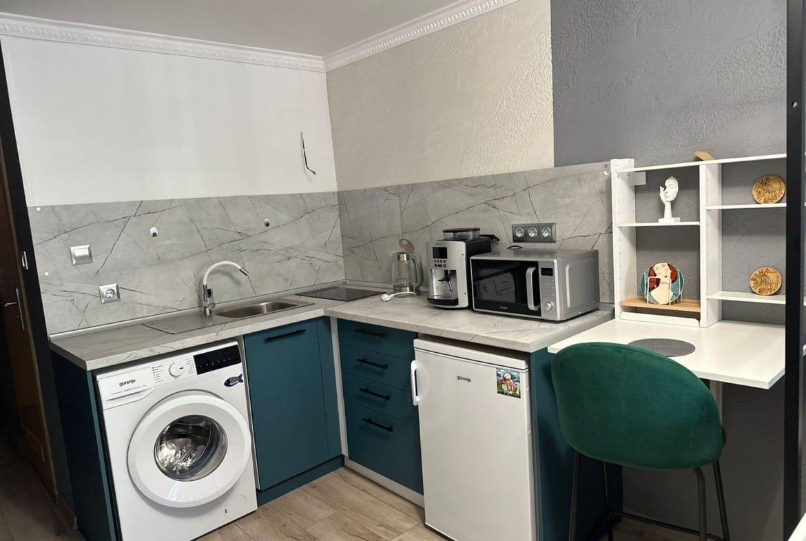 Современная кухня с стиральной машиной, холодильником и микроволновкой, оформленная в светлых и тёмных тонах, подходит для жилья в Болгарии.
