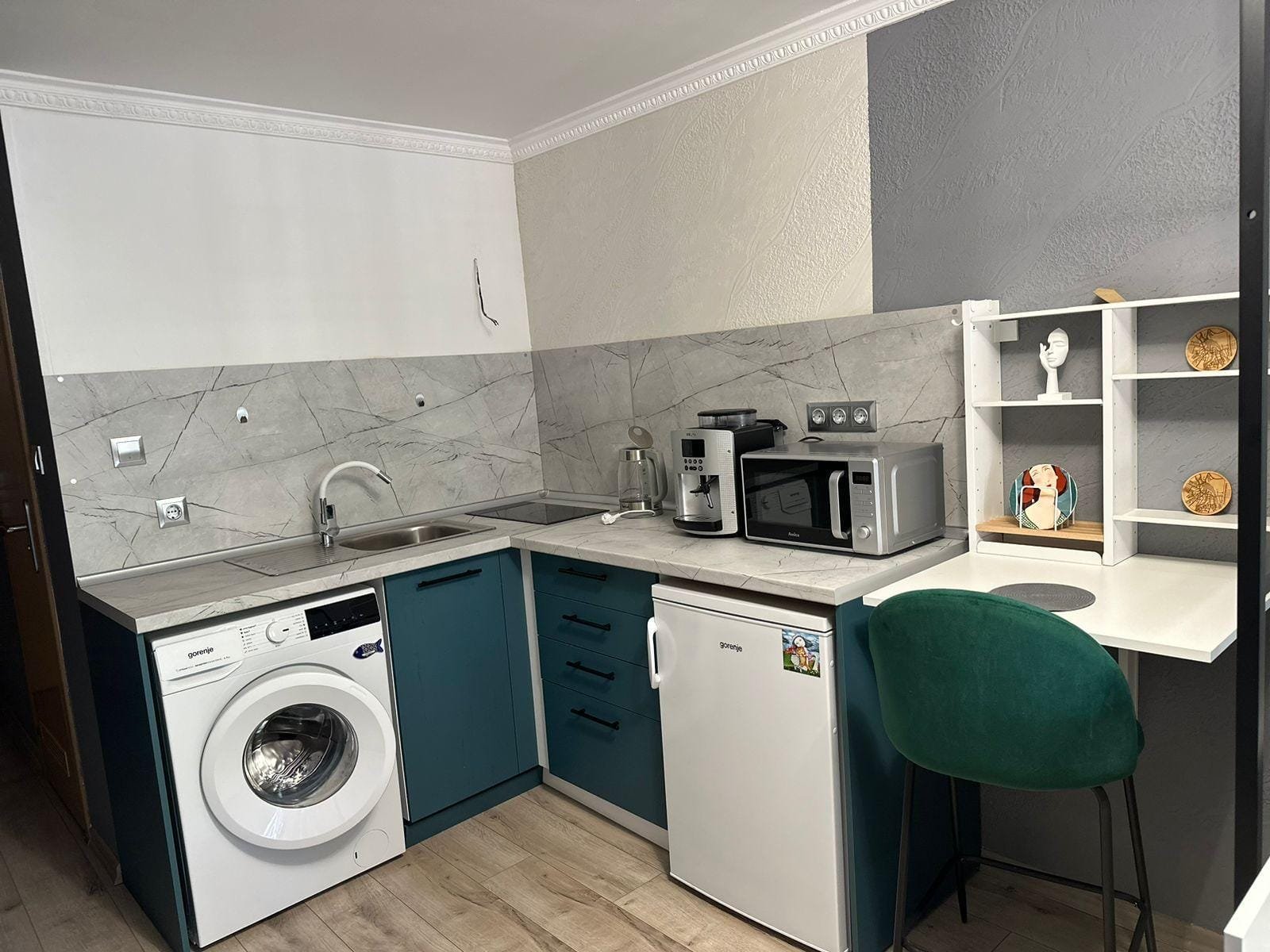 Современная кухня с стиральной машиной, холодильником и микроволновкой, оформленная в светлых и тёмных тонах, подходит для жилья в Болгарии.