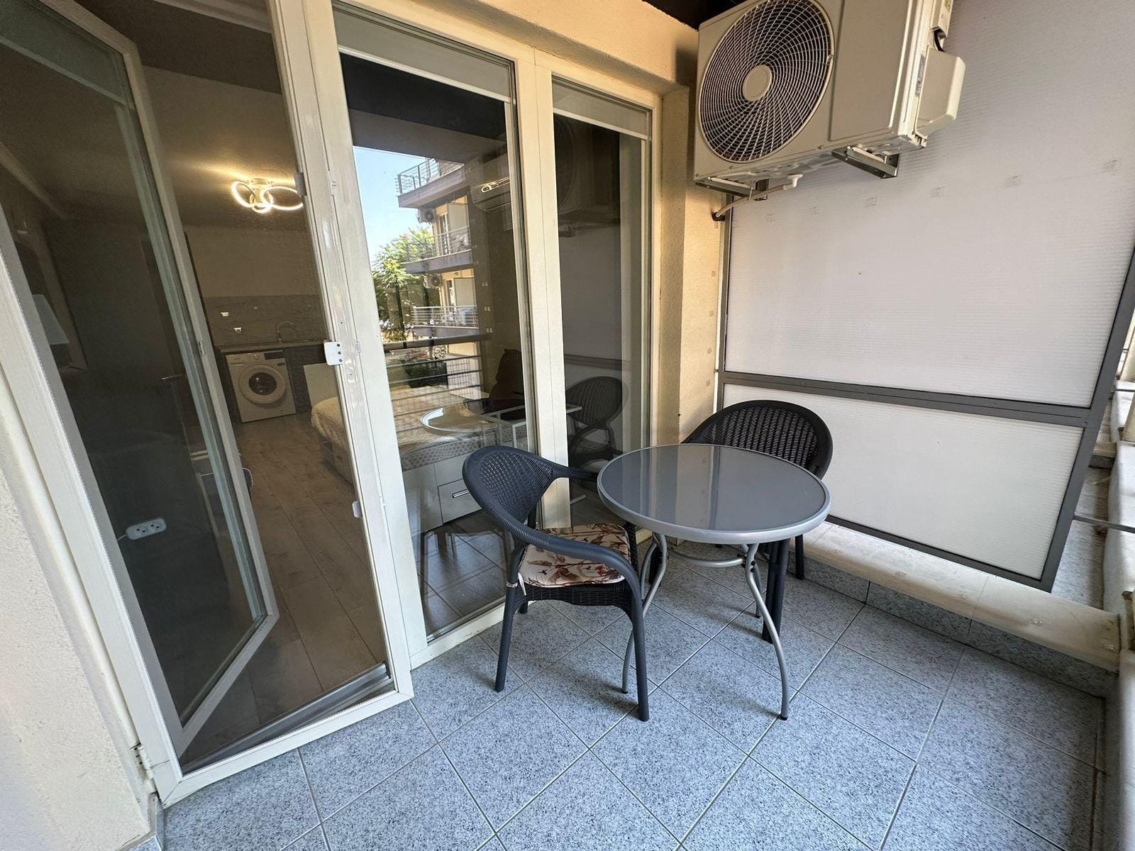 Современный балкон с круглыми столом и стульями, рядом кондиционер, светлое пространство, идеальное для отдыха в Болгарии.