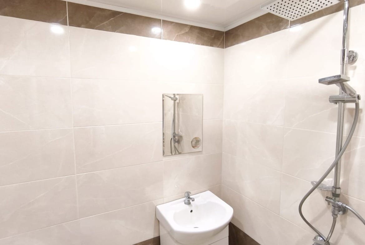 Современная ванная комната с душевой кабиной, белым умывальником и плиткой светлых тонов, идеально для жилья в Болгарии.