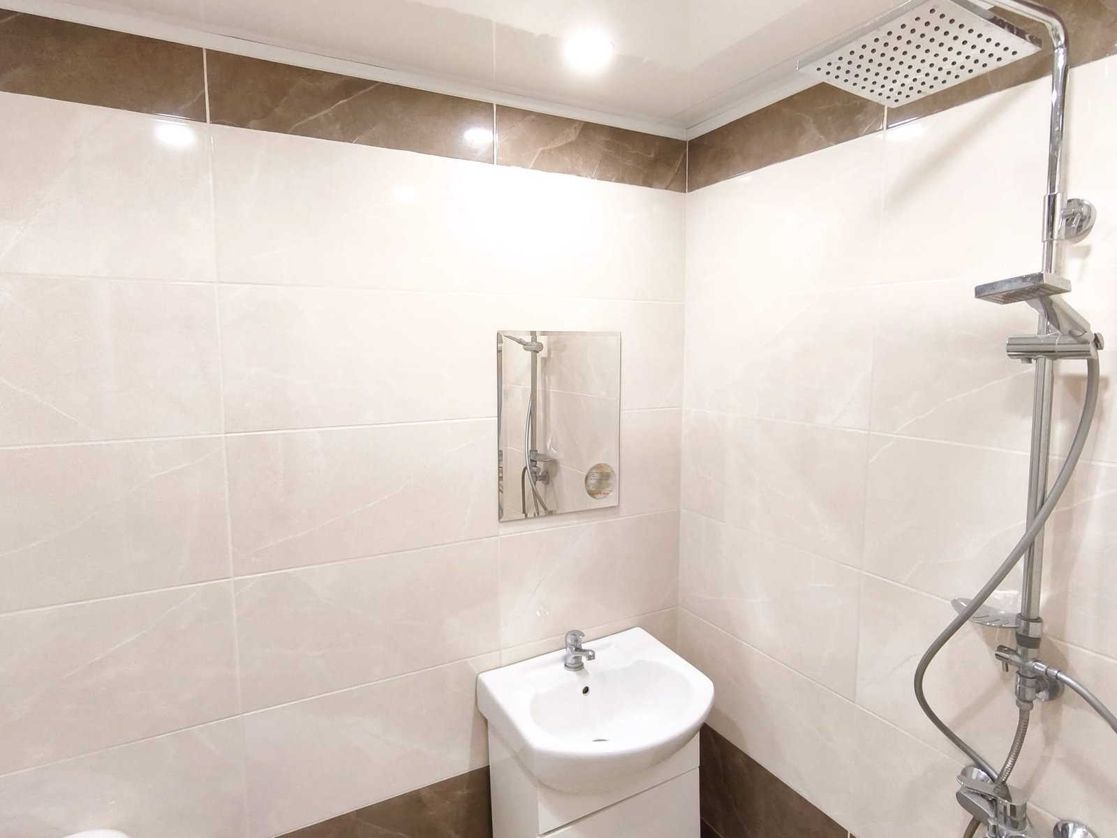 Современная ванная комната с душевой кабиной и раковиной Современная ванная комната с душевой кабиной, белым умывальником и плиткой светлых тонов, идеально для жилья в Болгарии.