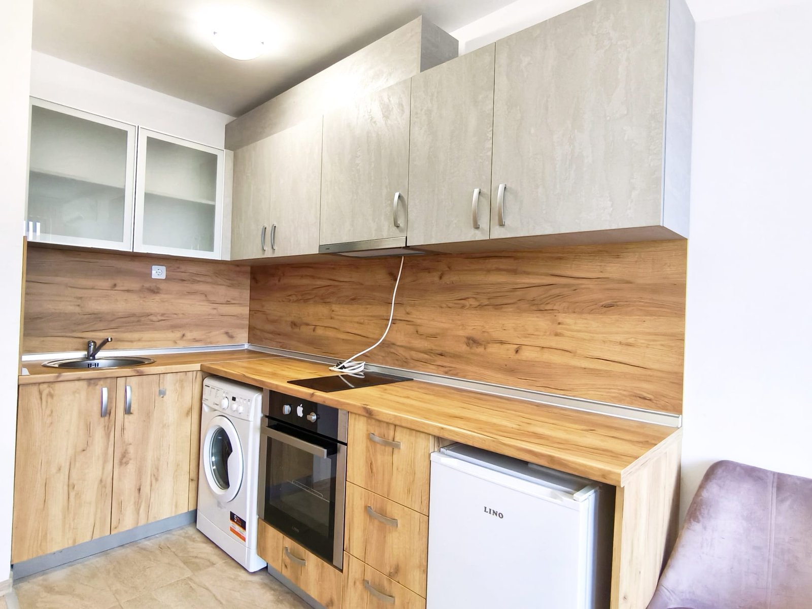 Современная кухня с бытовой техникой и деревянными фасадами Современная кухня в квартире в Болгарии, с древесными и светлыми фасадами, оборудована техникой для комфортной жизни.