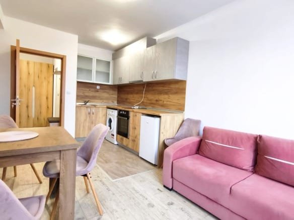 Современная кухня-гостиная с розовым диваном, деревянными фасадами и бытовой техникой, идеальна для аренды в Болгарии.