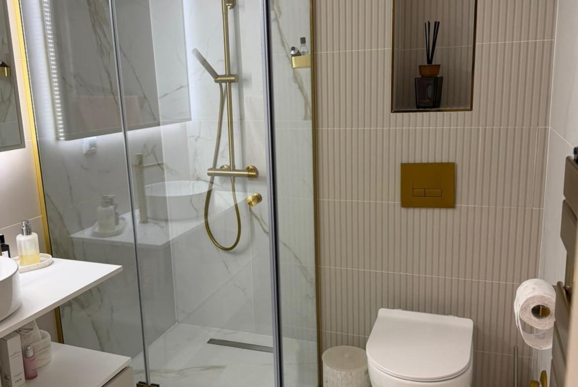 Современная ванная комната с душевой кабиной, золотыми элементами и стильным декором для успешной продажи недвижимости в Болгарии.